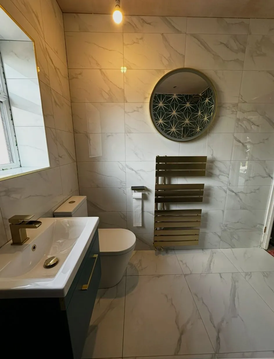 Basin and vanity unit with a marble-tiled wall, round mirror and a brushed brass heated towel rail