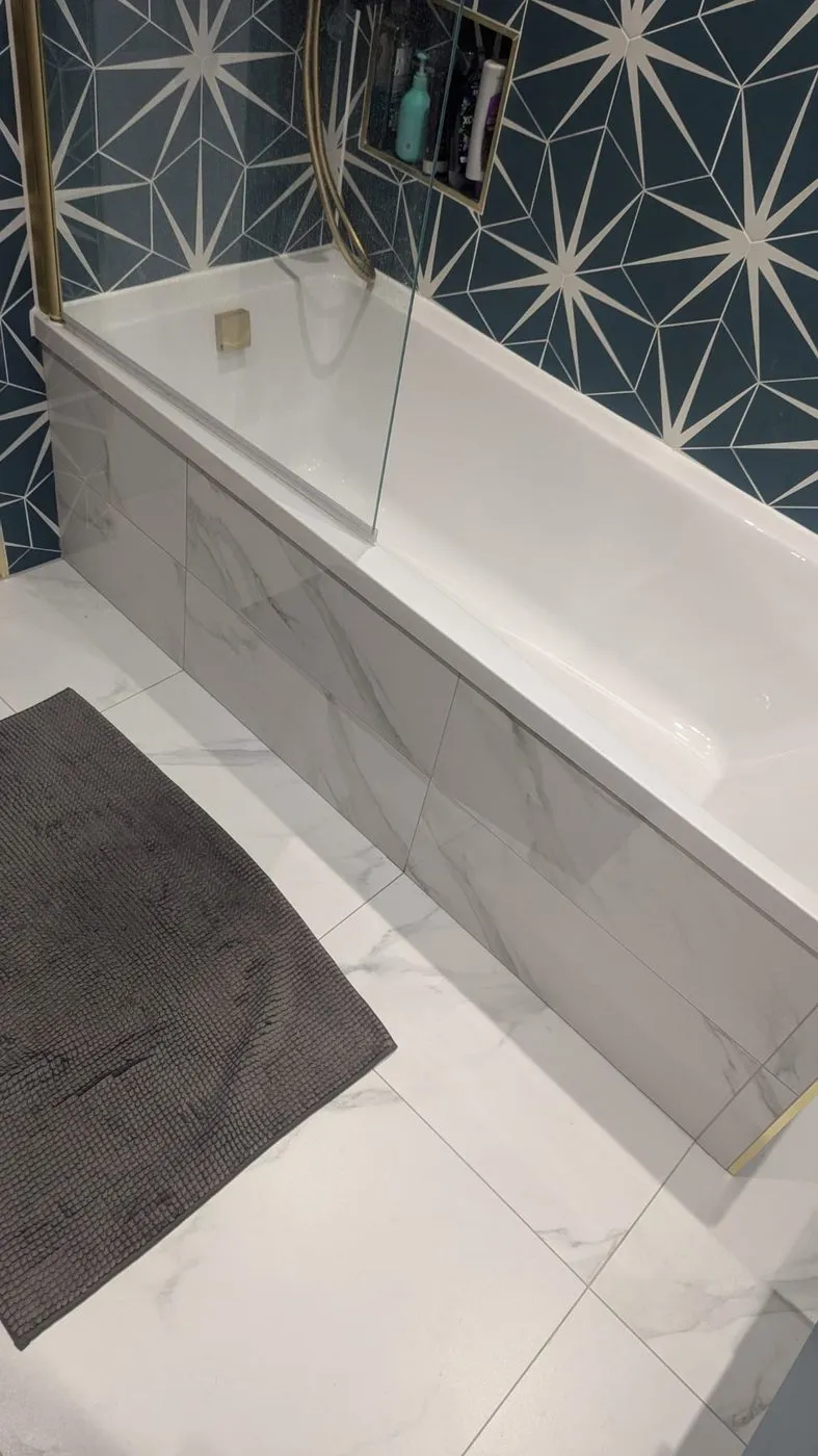 Bath with a marble-effect panel and glass shower screen, set against patterned green wall tiles