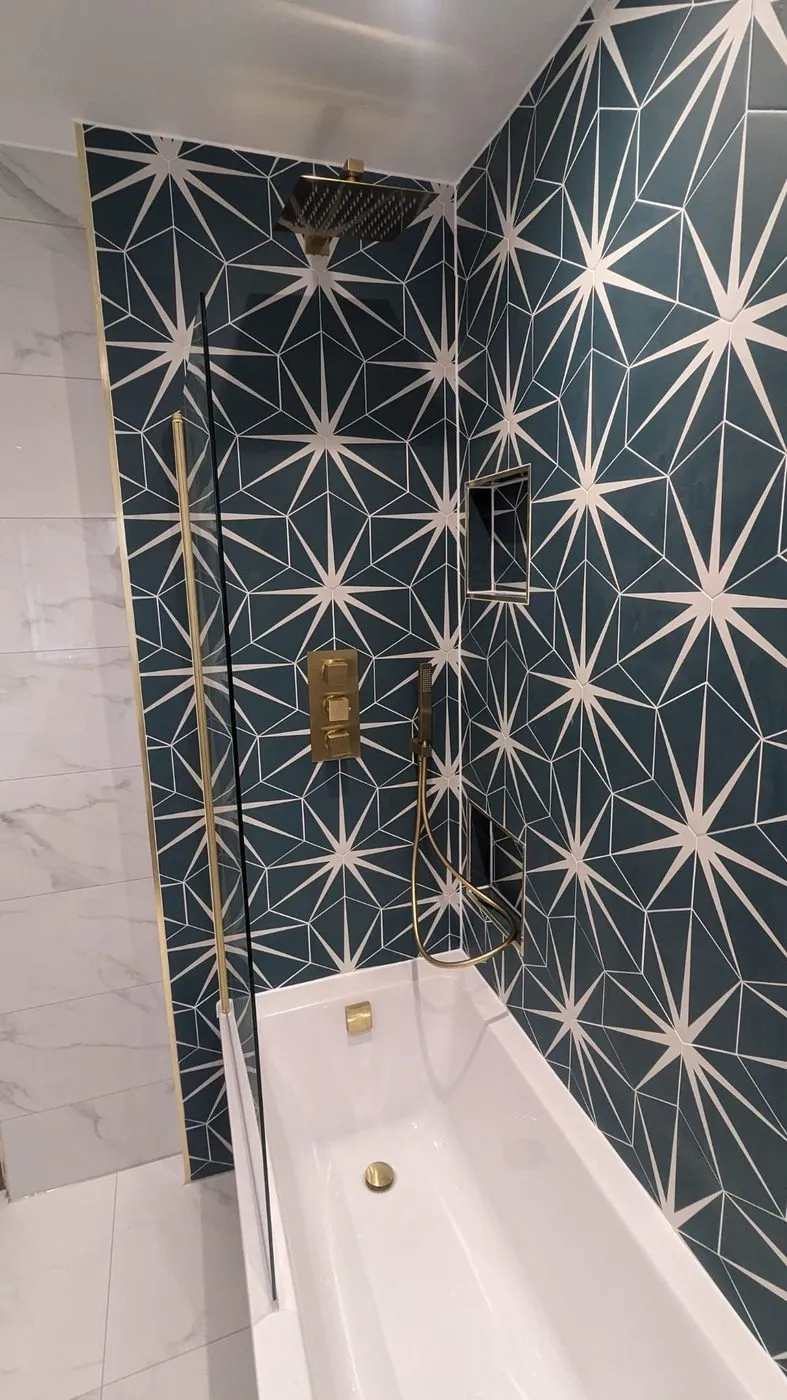 Shower over a white bath against dark green star-patterned tiles, with brushed brass shower valve and rail