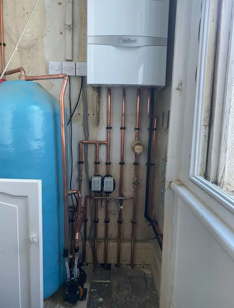 Vaillant boiler and cylinder in a utility space, with copper pipework, valves and a pump neatly run down the wall