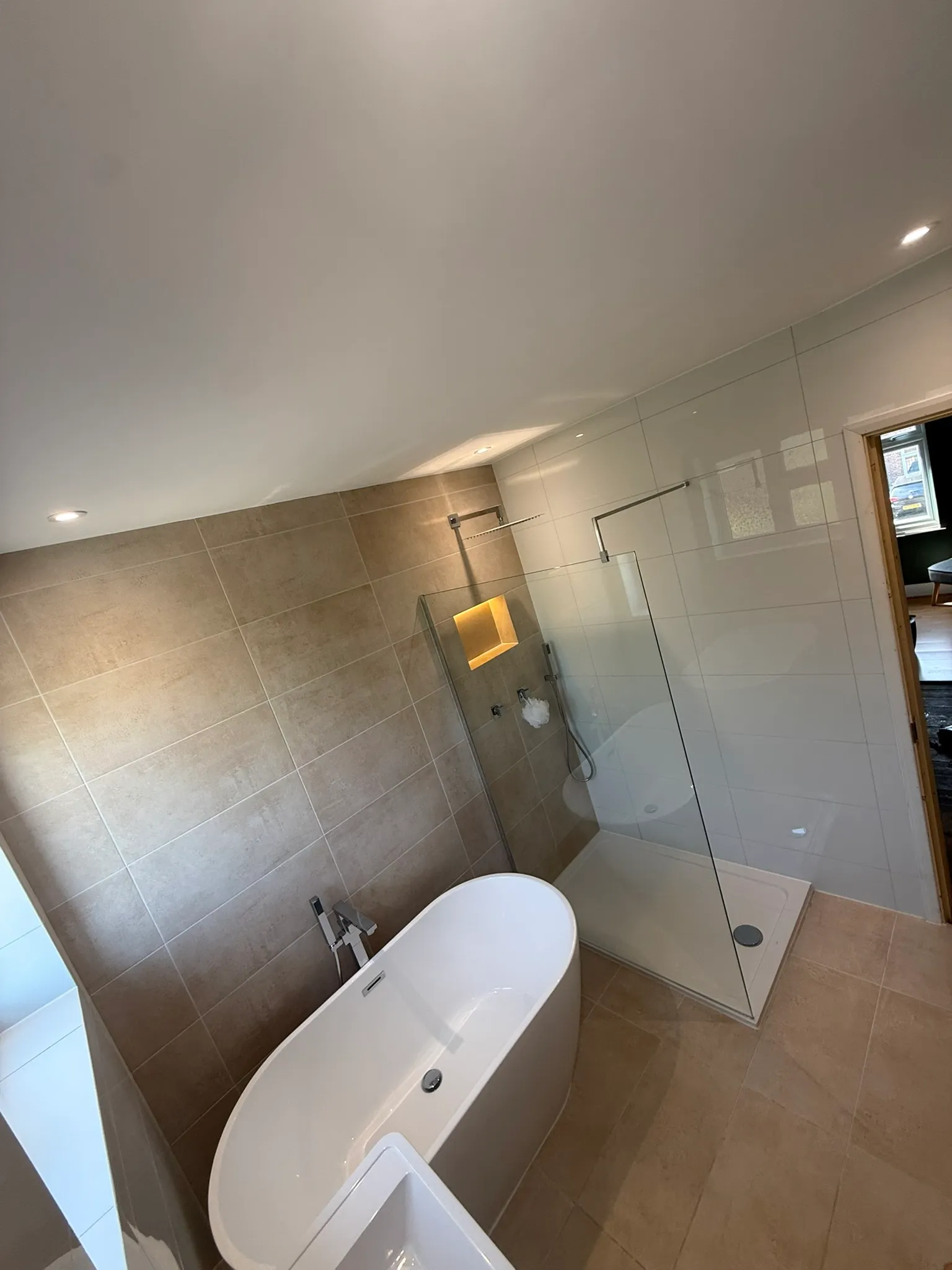 Walk-in shower in the same bathroom, with a rainfall head, glass screen, low-profile tray and a backlit niche set into large stone-effect tiles